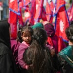 A gathering of Nepalese people celebrating with flags in a festive outdoor setting.