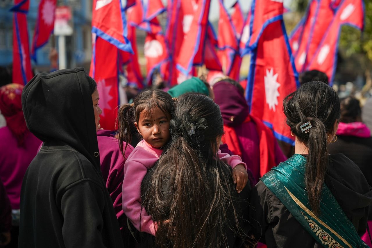 A gathering of Nepalese people celebrating with flags in a festive outdoor setting.
